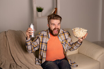 Bearded man watching film or sport games TV eating popcorn in house at night. Cinema, championship...