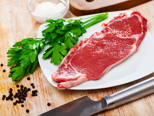 Piece of raw boneless beef on wooden background with seasonings and greens prepared for roasting