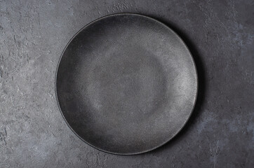 Dark grey textured concrete background for design with black food plate. Copy space