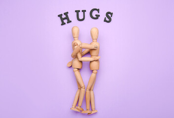 Wooden mannequins with word HUGS on color background
