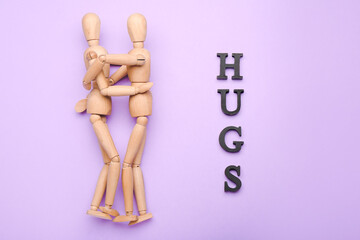 Wooden mannequins with word HUGS on color background