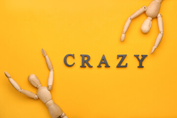 Wooden mannequins with word CRAZY on color background