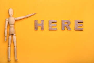 Wooden mannequin with word HERE on color background