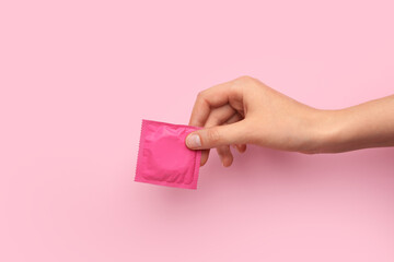 Female hand with wrapped condom on color background - obrazy, fototapety, plakaty