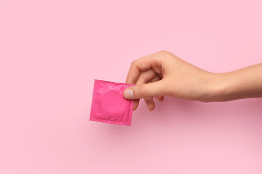 Female hand with wrapped condom on color background