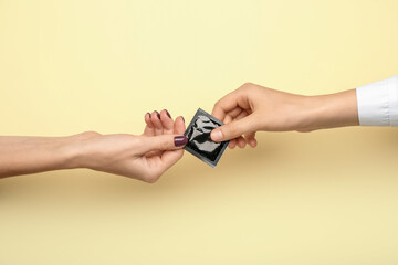 Female hands with wrapped condom on color background