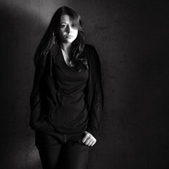 Outdoor portrait of a sad teenage girl looking thoughtful about troubles in front of a dark wall, copy space on the right side of the monochrome photo