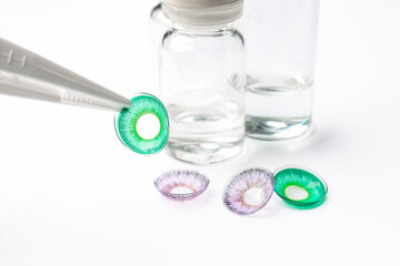 Tweezers with color contact lenses on white background