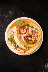 Tacos, tortillas with chicken meat, avocado, maize, and onion, top shot on a dark background