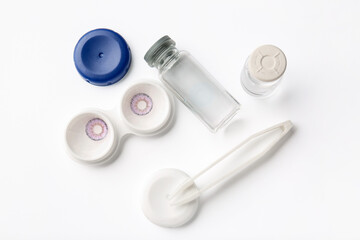 Container with color contact lenses and tweezers on white background