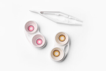 Containers with color contact lenses and tweezers on white background