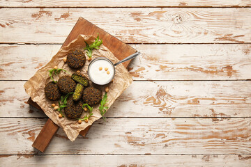 Board with tasty falafel balls and sauce on wooden background