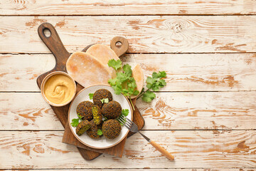 Plate with tasty falafel balls, sauce and pita on wooden background