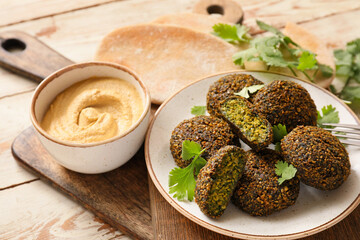 Plate with tasty falafel balls, sauce and pita on wooden background