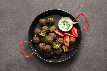Frying pan with tasty falafel balls, tomato and sauce on dark background