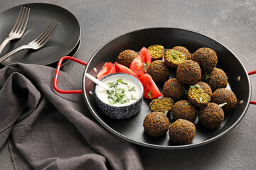 Frying pan with tasty falafel balls, tomato and sauce on dark background