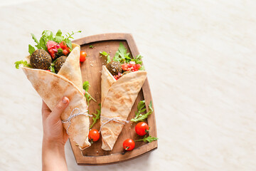 Female hand with tasty falafel pita on light background