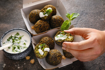 Woman eating tasty falafel balls with sauce on dark background