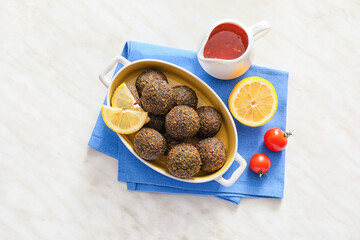 Baking dish with tasty falafel balls, lemon and sauce on light background