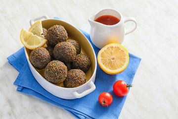 Baking dish with tasty falafel balls, lemon and sauce on light background