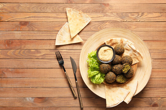 Plate with tasty falafel balls, pita and sauce on wooden background