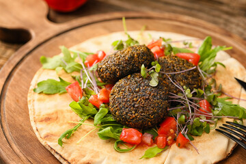 Board with tasty falafel balls, pita and vegetables on wooden background