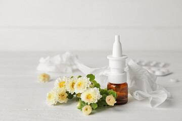 Bottle with drops, flowers and used tissue on light background