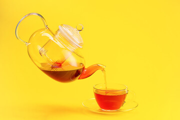 Pouring of hot tea from teapot into cup on color background