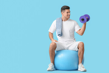Sporty young man training with dumbbell on color background