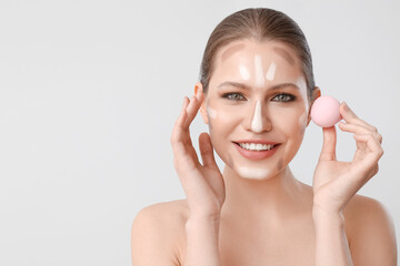 Beautiful young woman applying contouring makeup against light background