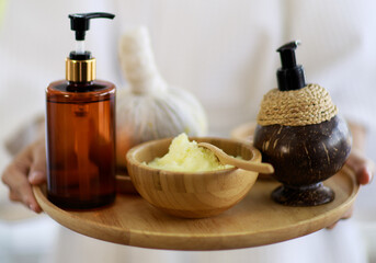 Spa massage therapy equipment are herbal compress ball, massage herbal oil is put on a wood plate, and blurred pink flower shoot on morning light