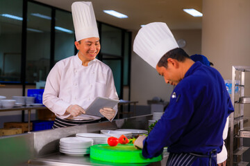 An Asian male chef hold tablet control his team while foods preparation in the kitchen.