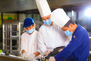 An Asian male chef hold tablet control his team while foods preparation in the kitchen.