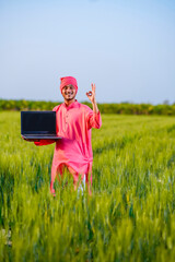 Young indian farmer showing laptop screen at wheat field