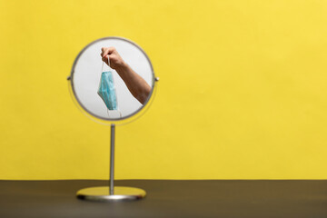 A round mirror, with a medical mask on it, on a yellow background.
