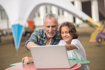Son and dad sitting together with a laptop and looking contented