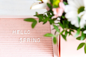 Hello Spring greeting message sign on pink felt board with blooming flowers on white background. board with text for social media blogs banner. Green leaves, natural floral bloom decoration.