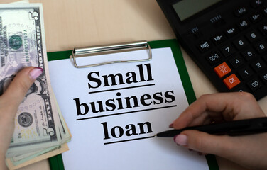 SMALL BUSINESS LOAN - word in a folder against the background of women's hands with a house and...
