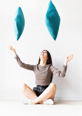 Beautiful happy woman in casual clothes sitting on the floor throwing pillows into the air