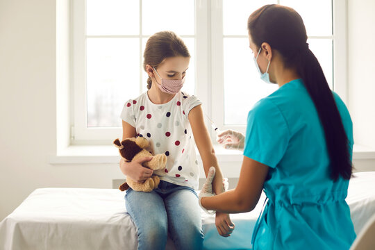 Professional Nurse Giving Shot To Little Kid. Doctor Injecting Child With Flu Or Covid 19 Vaccine. Girl In Medical Face Mask Holding Favorite Toy And Getting Injection At Clinic. Immunization Concept