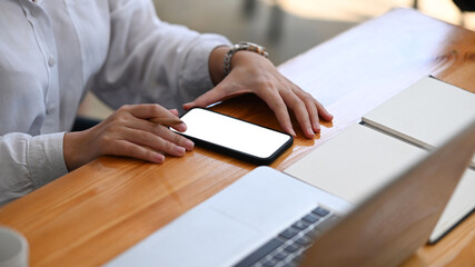 Cropped shot of businesswoman using mobile phone on wooden office desk.