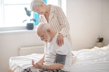 Obraz premium Grey-haired elderly woman helping her husband to check blood pressure