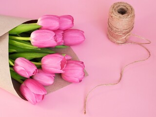 Pink tulips in craft paper on pink background. Florist preparing bouquet of fresh beautiful tulips. Easter, Valentine's Day, Mother's day. Spring card. Place for text. Minimalism