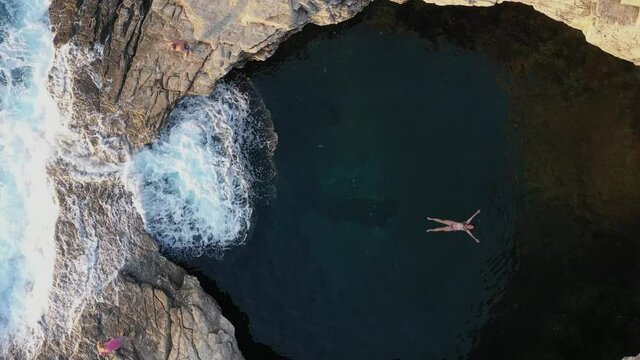  Above aerial view of a girl floating and swimming in Giola lagoon, natural pool near the sea, in Thassos island, Greece