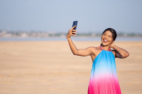 beautiful young african lady taking pictures with her phone on the beach