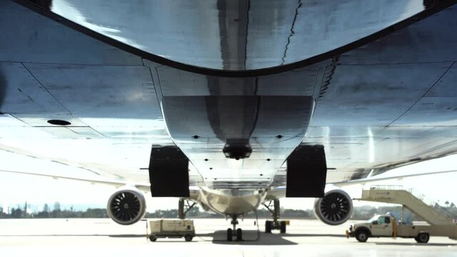 Bottom of a commercial aircraft with the beacon light flashing. Aircraft and ground equipment in the background.
