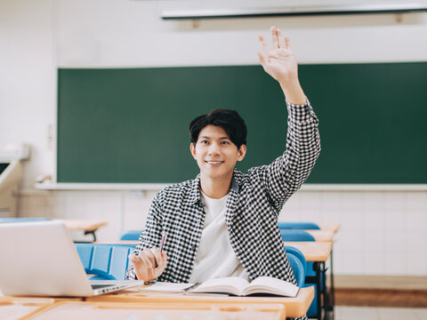 Young Cheerful Asian Student Raising Hand In Classroom