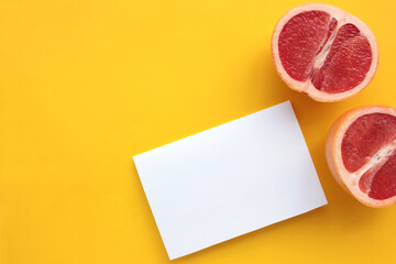 Summer still life with half of grapefruit and blank paper card on yellow background. Invitation...