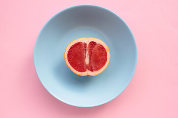 Half of grapefruit on a blue plate on a pink background. Top view, copy space.

