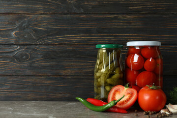 Jars with pickled tomatoes and cucumbers on wooden background